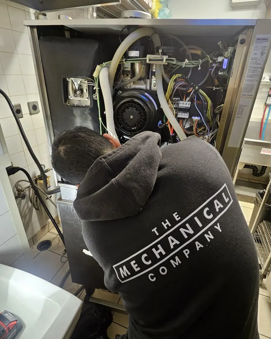 A Mechanical Company technician repairing a Rational combi oven in a commercial kitchen